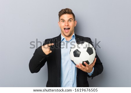 Young soccer trainer surprised pointing at himself, smiling broadly.