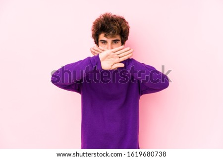 Young caucasian man against a pink background isolated doing a denial gesture