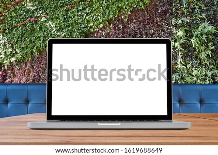 Laptop on wooden desk against ecological foliage wall