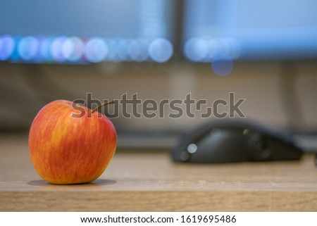 A red apple on office desk on computer screen blurred background.