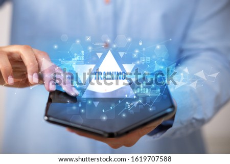 Businessman holding a foldable smartphone with TRAINING inscription, business concept