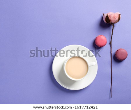 minimalistic picture of a cup of coffee, macarons and cotton flower on a delicate lilac background. creative breakfast. flat lay, copy space.
