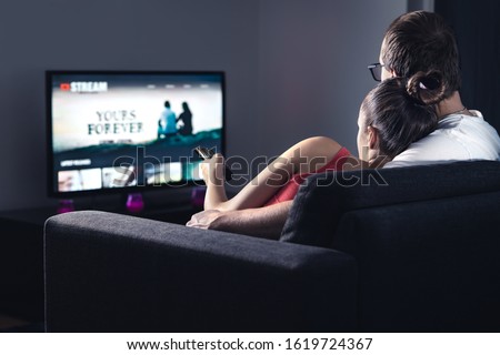 Movie stream service on smart tv. Couple watching series online. Woman choosing film or new season with remote control. Video on demand (VOD) site mockup on screen. Digital streaming network. Royalty-Free Stock Photo #1619724367