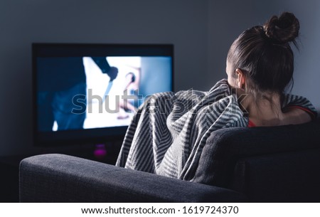 Scary horror movie on tv. Scared woman watching stream service hiding under blanket on couch at night. Sleepless person streaming series or film on television. Alone in dark and afraid of thriller. Royalty-Free Stock Photo #1619724370