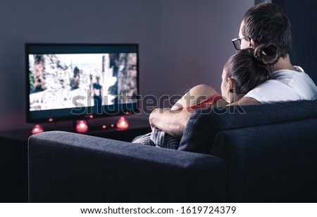 Couple watching movie or series. Online streaming and VOD service in tv screen. Film stream or television show. Cuddling during comfy and romantic candle light date at home. Man and woman relaxing. Royalty-Free Stock Photo #1619724379