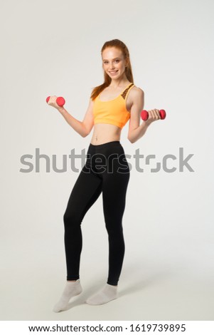 beautiful young woman with red hair on a white background with dumbbells in hands