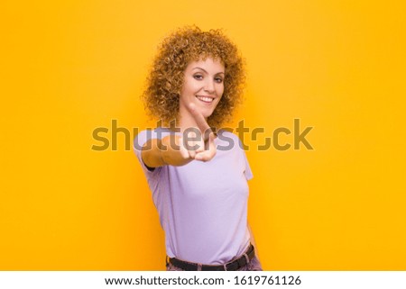 young afro woman smiling proudly and confidently making number one pose triumphantly, feeling like a leader against orange wall