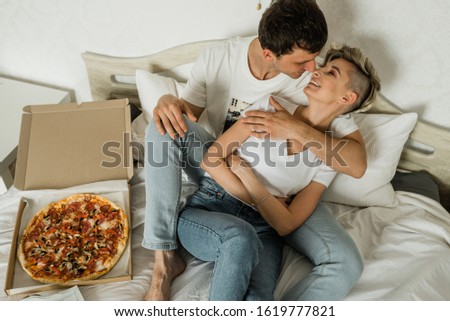 Beautiful young couple with pizza while lying on the bed at home