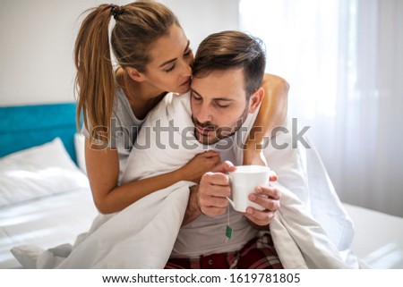 Woman taking care of his boyfriend. Couple sitting on sofa, ill man with blanket over his body and woman taking care. Woman taking care of her sick boyfriend lying on the sofa