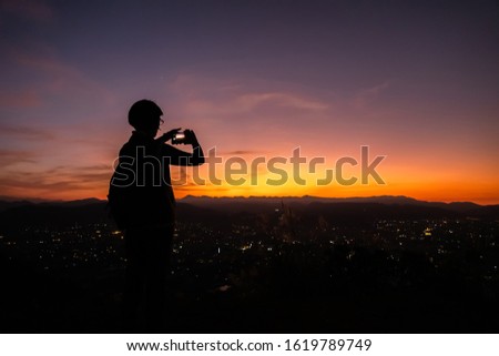 silhouette of traveling woman take a photo by smartphone at the top of a hill in city