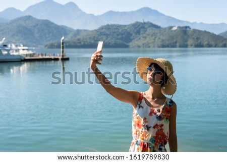 traveling mature Asian woman selfie by mobile phone at Sun Moon Lake, Taiwan