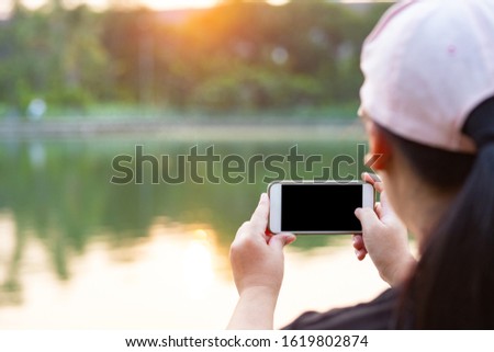 Rear view of woman holding smart phone for taking photo in the evening with clipping path on screen 