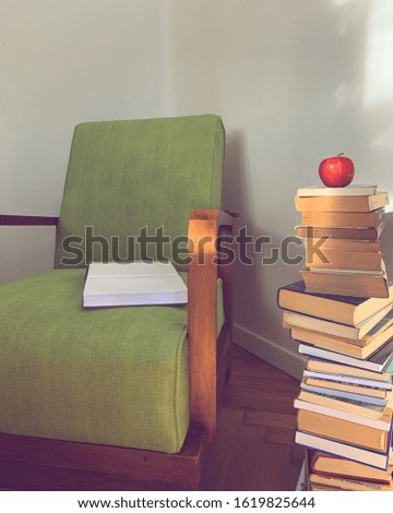 Red apple on the top of the stack of old books and vintage armchair