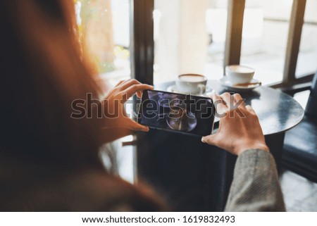 A woman using mobile phone to take a photo of coffee and snack before eat