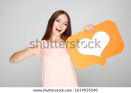 Young woman holding paper card with heart on grey background