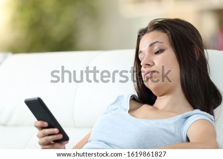 Bored girl checking mobile phone sitting on a couch in the living room at home