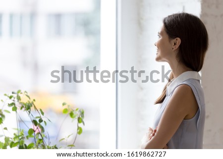 Happy millennial business woman standing indoors with arms crossed looking out the window daydreaming, female visualizing thinking planning future successful project and deal. Business vision concept Royalty-Free Stock Photo #1619862727