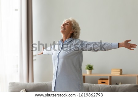 Happy older woman with toothy healthy smile standing with arms outstretched in living room at home, thankful grateful mature female feeling satisfied, doing easy exercises, stretching, enjoying life Royalty-Free Stock Photo #1619862793