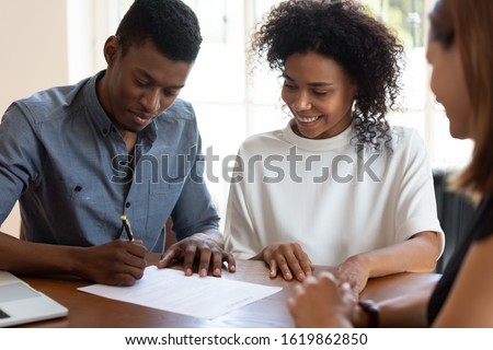Happy African American family signing contract, legal documents, satisfied clients making deal with realtor or broker, smiling couple wife and husband purchasing new house, taking loan or mortgage