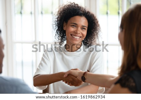 Smiling African American businesswoman shaking hand of client at meeting, friendly realtor broker manager making deal with family, customers purchasing new house, taking loan or mortgage in bank Royalty-Free Stock Photo #1619862934