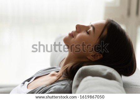 Close up head shot profile peaceful beautiful woman relaxing, sleeping on comfortable couch at home, pretty young female enjoying rest, weekend, breathing fresh air, meditating with closed eyes Royalty-Free Stock Photo #1619867050