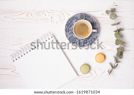 Composition from an empty diary with a spring, a cup of coffee and macaroons and a branch of eucalyptus on a white shabby wooden table. Fashion flat lay.