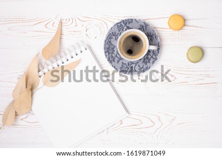 Composition from an empty diary with a spring, a cup of coffee and macaroons and beige leaves on a white shabby wooden table. Fashion flat lay.