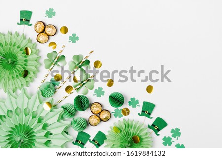 Decorations and props for St.Patrick 's Day party. Green and gold paper decorations, hat, balloons, confetti, candy and lucky symbols on white background. Festive concept. Flat lay, top view.