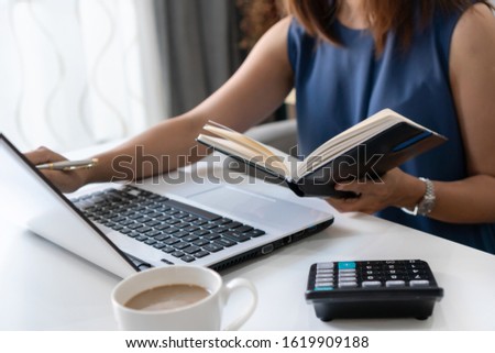 Pretty young Asian businesswoman working with computer laptop while looking at financial documents in notebook. Home office concept