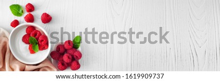 Healthy yogurt with raspberries. Banner with corner border against a rustic white wood background. Copy space.