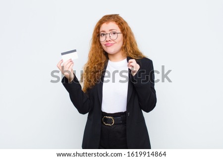 red head young woman looking arrogant, successful, positive and proud, pointing to self against white wall