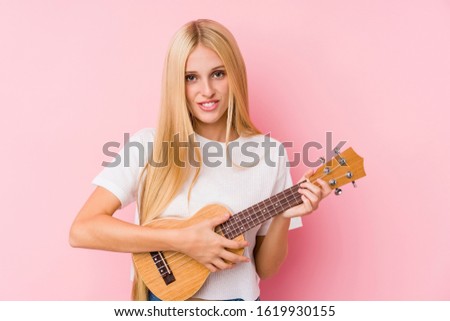 Young blonde woman playing ukelele isolated in a background