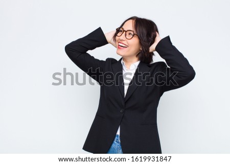 young businesswoman smiling and feeling relaxed, satisfied and carefree, laughing positively and chilling against white wall