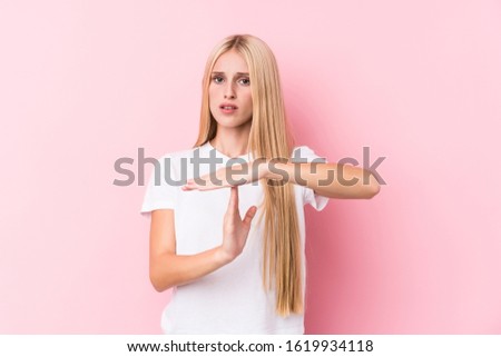 Young blonde woman on pink background showing a timeout gesture.