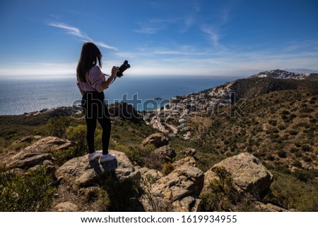 Beautiful woman photographer standing on a cliff holding a professional camera with the mediterranean sea in the background in Spain with copy space