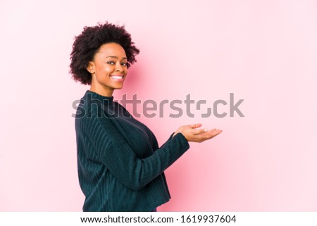 Middle aged african american woman against a pink background isolated holding a copy space on a palm.