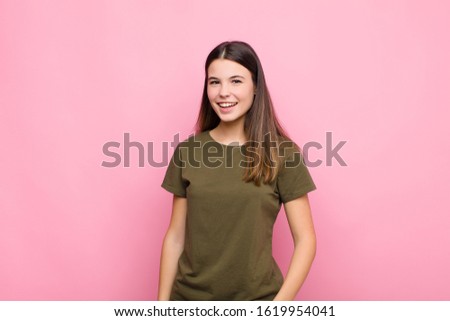 young pretty woman with a big, friendly, carefree smile, looking positive, relaxed and happy, chilling against pink wall
