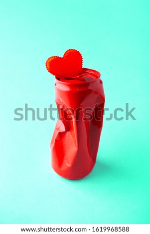 Creative Valentine's day background with a red crumpled metal soda can  and one fabric heart on a turquoise background