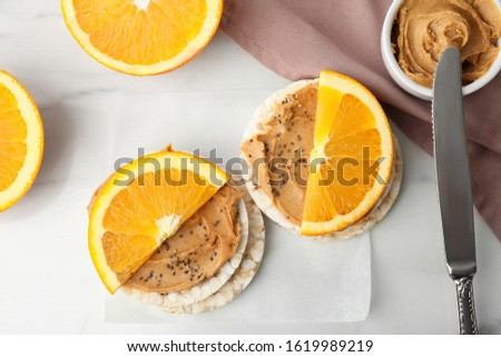 Puffed rice cakes with peanut butter and orange on white marble table, flat lay