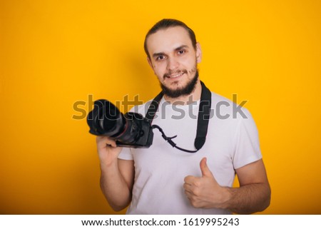 Photographer on a yellow background. The guy is holding a camera. Process work. Photographs in the studio