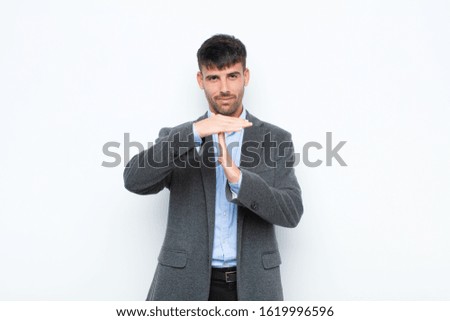 young handsome man looking serious, stern, angry and displeased, making time out sign against white wall