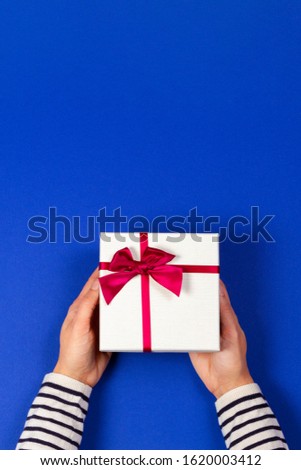 Woman hands holding present gift box tied with ribbon on navy blue background. Top view, place for text. Holiday concept