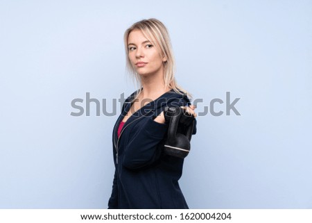 Young sport blonde woman over isolated blue background making weightlifting with kettlebell