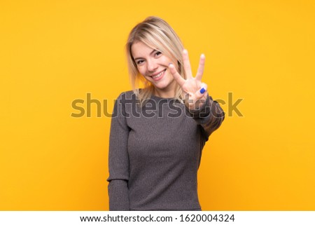 Young blonde woman over isolated yellow background happy and counting three with fingers