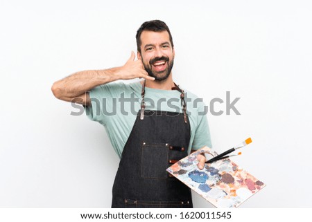 Young artist man holding a palette over isolated background making phone gesture. Call me back sign