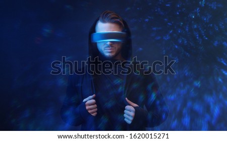 Young man in hoodie on virtual reality background. Guy using VR helmet. Augmented reality, future technology, game concept. Blue neon light.
