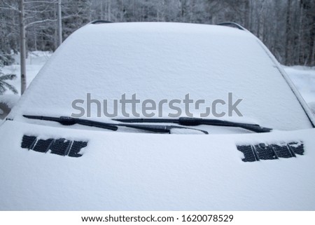 Snow covered car in the winter forest. The windshield is covered with snow.