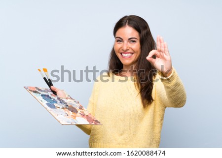 Young artist woman over isolated blue background showing ok sign with fingers