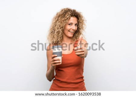 Young blonde woman with curly hair holding a take away coffee with thumbs up because something good has happened
