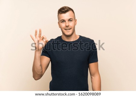 Young handsome blonde man over isolated background surprised and showing ok sign